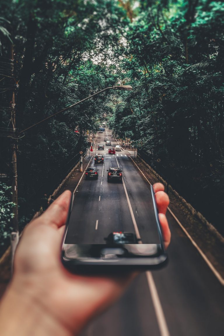 a person holding a phone up to a window with a city in the background