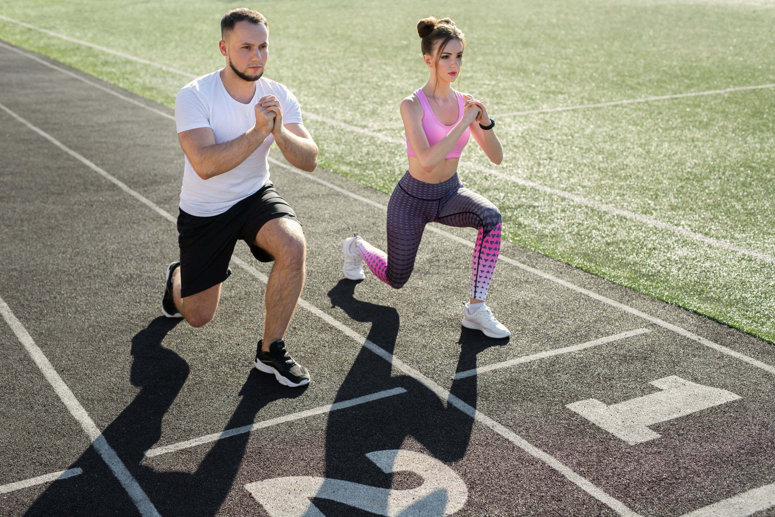 Man and a woman play sports at the stadium in the summer, making lunges.